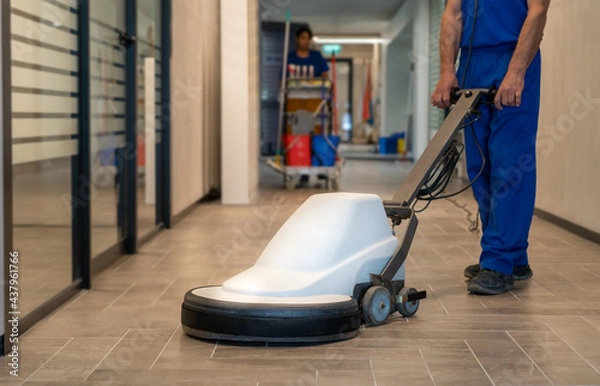 Fototapeta Professional cleaner polish hard floor with high speed machine.Cleaning leady with trolley is in the background