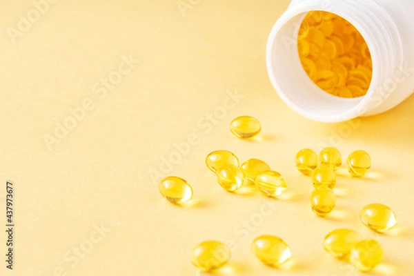 Fototapeta Fish oil soft gel supplement capsules source of omega 3 and vitamins A, E on yellow background near pharmaceutical bottle close-up. Copy space