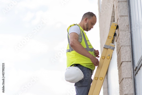 Fototapeta telecommunications technician climbing to the top of a ladder without a safety helmet on