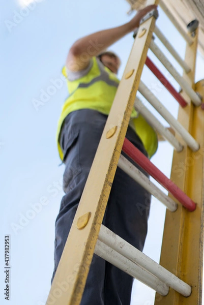 Fototapeta technician working on a yellow ladder
