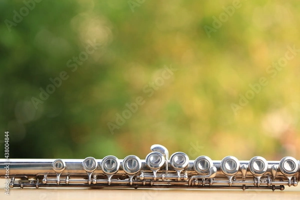 Obraz Flute, woodwind brass instrument in classical orchestra. Silver modern flute on white sheet music note for education and performance. Song composer on score sheet with green bokeh nature.