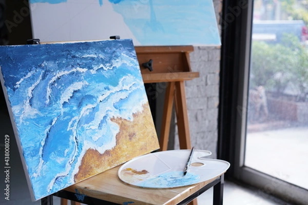 Fototapeta Acrylic sea and beach painting on drawing stand with palette and brush. Blue wave on golden sand hand painting with brush and knife palette technique. Art on canvas.