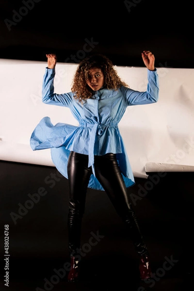 Fototapeta vertical portrait of a curly model wearing a blue dress and black latex pants with black and white paper like background