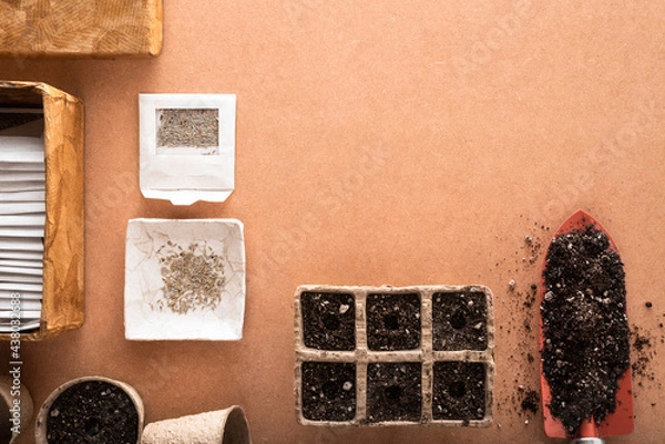 Fototapeta Lettuce seeds and many other vegetable seeds in small envelopes with a shovel and peat pots and trays full of potting soil ready for sowing, on a raw surface with space for text