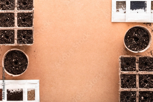 Fototapeta Biodegradable peat pots and trays full of potting soil made of peat, worm humus and perlite, and many vegetable seeds in small envelopes ready for sowing, on a raw surface with copy space