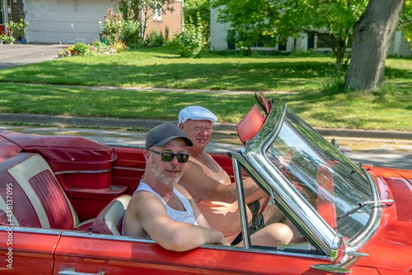 Fototapeta Father and son going for a Sunday drive in an old 1960s red convertible.