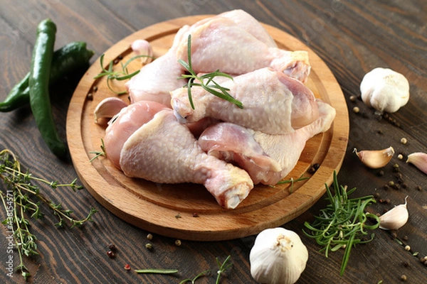 Obraz Raw chicken legs with spices on a board on a wooden table