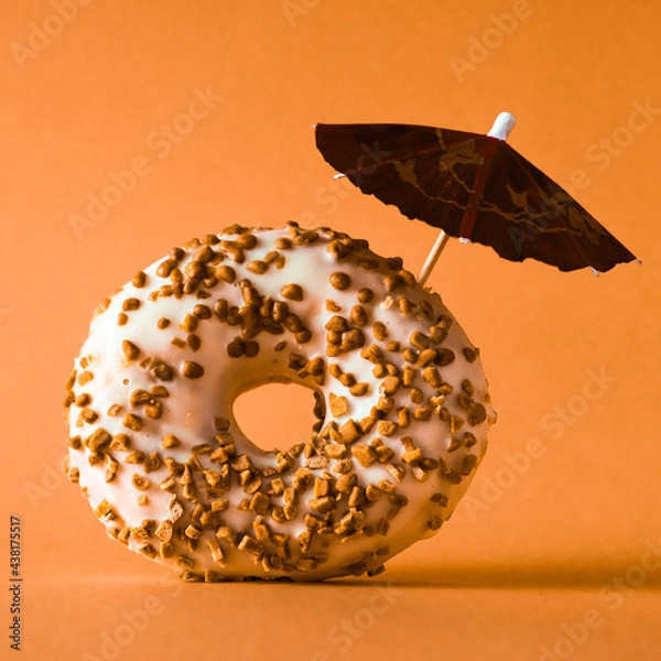 Fototapeta White chocolate donut with almonds topping and a decoration umbrella on orange background.