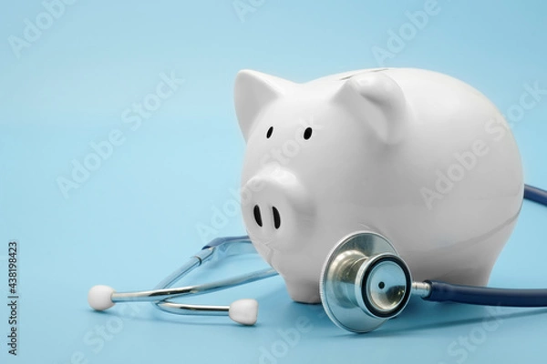 Fototapeta Piggy bank with stethoscope isolated on light blue background with copy space. Health care financial checkup or saving for medical insurance costs concept.