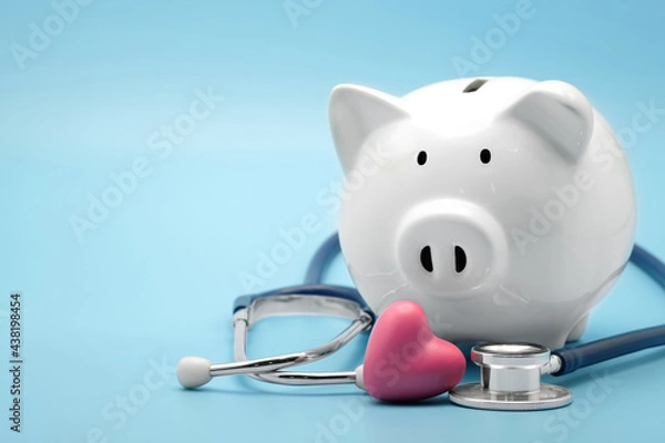 Fototapeta Piggy bank with stethoscope and heart isolated on light blue background with copy space. Health care financial checkup or saving for medical insurance costs concept.