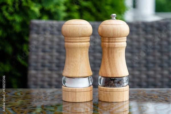 Obraz Salt and black pepper shakers in a summer cafe, a wooden pepper mill on a table in a restaurant. Spices, ingredients in cooking.