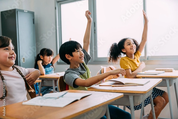 Obraz Elementary age Asian student boy raised hands up in class. Diverse group of pre-school pupils in elementary age in education building school. Volunteering and participating classroom concept.