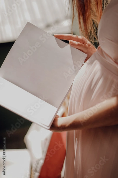Fototapeta Pregnant woman read with white book mockup in hand on shine background