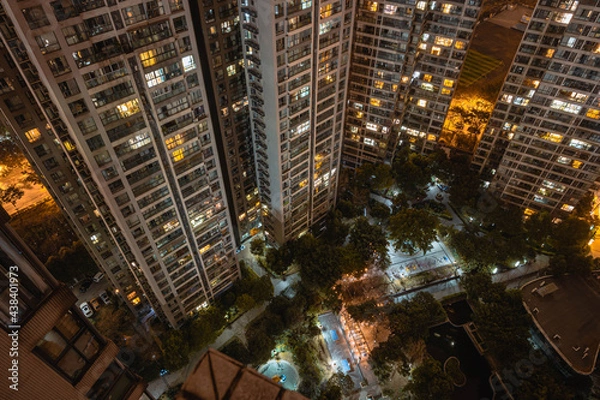 Fototapeta Long exposure night aerial view on residential buildings complex compound. Tall skyscrapers thousands of apartments light illuminates from windows. Small square park inside community. City development