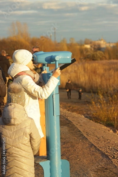 Fototapeta A girl looks through panoramic binoculars on a viewing platform in autumn park.