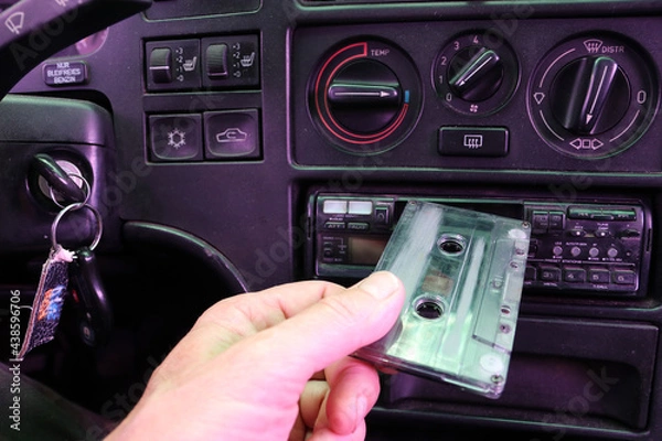 Fototapeta The driver inserts a cassette into a cassette recorder in an old car.