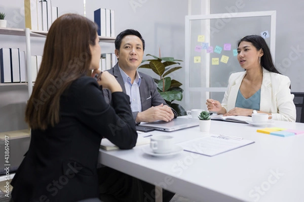 Fototapeta Motivated middle-aged Asian businessman and two young businesswomen happily exchanged ideas for business plans, enjoying working together at the office. leadership workplace.