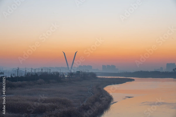 Fototapeta The silhouette of a building with the light of dawn and a river flowing through it
