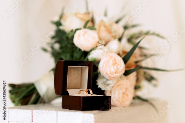 Obraz Wedding gold rings in a box next to a bouquet, on a light background.