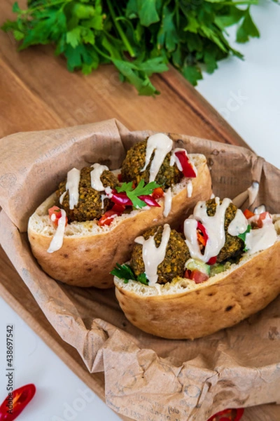 Obraz Authentic fresh falafel balls inside of two halves of pita bread sandwich with chopped salad, red hot peppers, lemon, a drizzle of tahini sauce. chickpea falafel in a fluffy pita on a wooden board