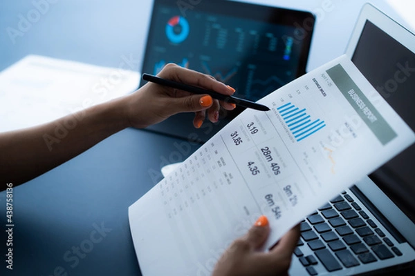 Fototapeta Asian business woman reviewing data in financial charts and graphs with tablet. Accounting