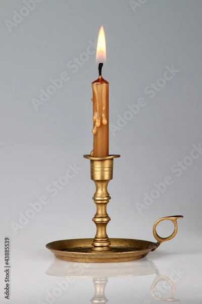 Fototapeta Lighted candle in an old brass candlestick, with a gray backgrou