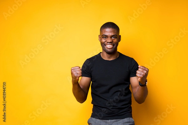 Fototapeta Happy african american man rejoices in victory clenching his hands into fists and smiling broadly