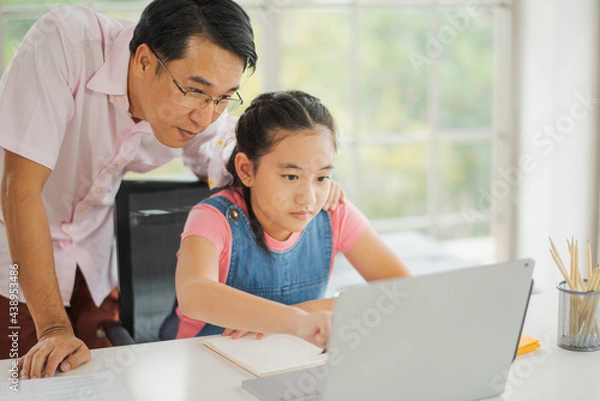Fototapeta Young Asian love family daughter learning online use computer notebook and father help to teach in living room at home which smiling and felling happy. live at home concept in COVID-19 situation