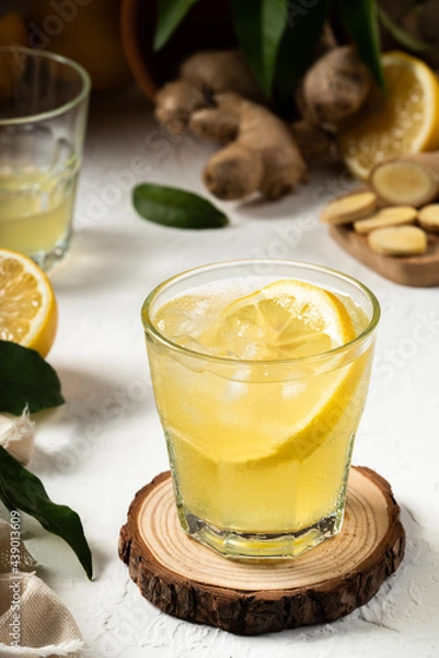 Fototapeta Detox and fresh lemon drink with ginger and a slice of lemon inside the glass, as an immune boosting and weight loss drink, on a white textured surface, soft light