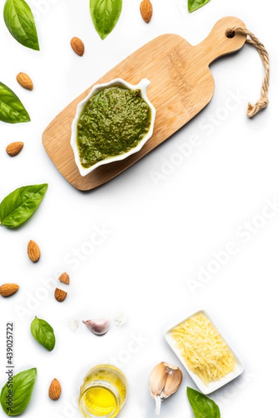 Fototapeta Green pesto sauce made of basil, almonds, garlic, parmesan cheese and olive oil, in a leaf-shaped porcelain bowl and a small wooden table, on a pure white surface with copy space