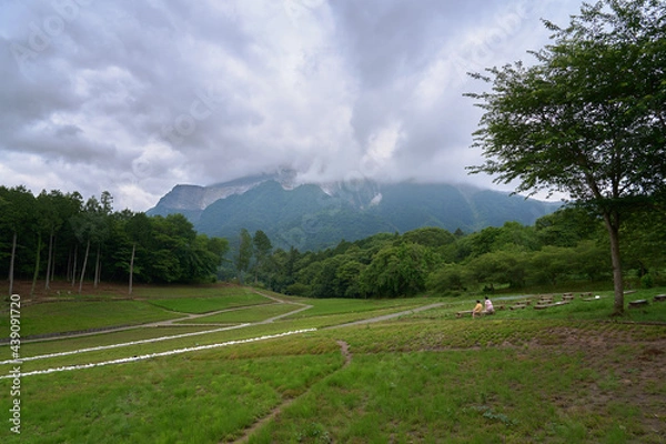 Fototapeta Two people relaxing in a field where you can see a mountain covered with clouds
