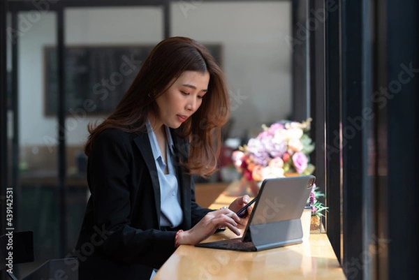 Fototapeta Asian businesswoman sitting at the counter working using a tablet in hand holding a smartphone at the office.