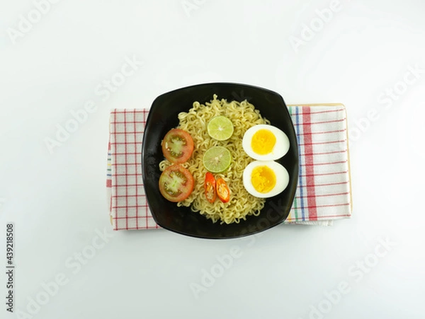 Fototapeta Indonesian noodle With a black bowl with eggs and fresh tomatoes on a napkin base on a white background