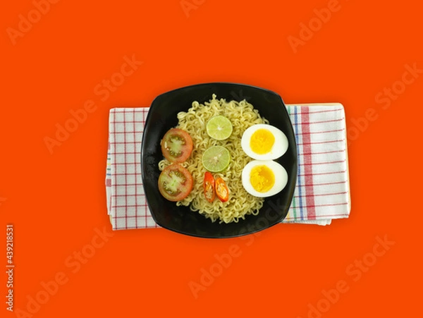 Fototapeta Indonesian noodle With a black bowl with eggs and fresh tomatoes on a napkin on a red background
