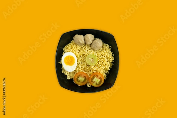 Fototapeta Indonesian Warm noodles served with eggs and fresh tomatoes with meatballs on a black bowl and pickled on a white bowl on a white background