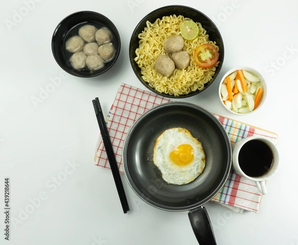 Fototapeta Indonesian Warm noodles served with eggs and fresh tomatoes with meatballs on a black bowl and pickled on a white bowl and eggs on a white background