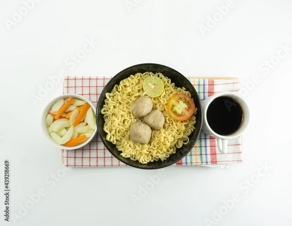Fototapeta Indonesian Warm noodles served with fresh tomatoes and meatballs in a round bowl on black and pickles on a white bowl on a white background