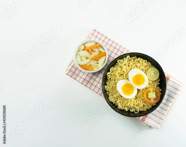 Obraz Indonesian Warm noodles served with fresh tomatoes and meatballs in a round bowl on black and pickles on a white bowl on a white background
