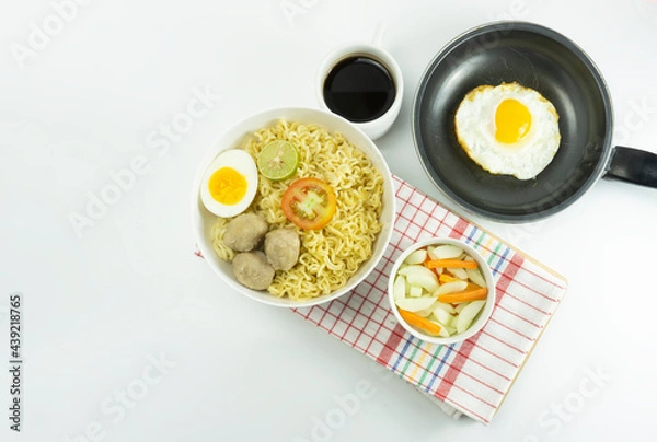 Obraz Indonesian Warm noodles served with fresh tomatoes and meatballs on a white round bowl and pickles on a white bowl on a white background