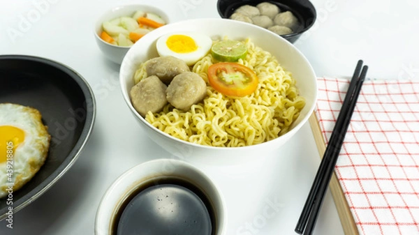 Fototapeta Indonesian Warm noodles served with fresh tomatoes and meatballs on a white round bowl and pickles on a white bowl on a white background