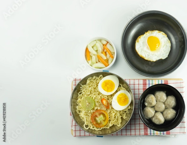 Fototapeta Indonesian Warm noodles served with fresh tomatoes and meatballs on a white round bowl and pickles on a white bowl on a white background