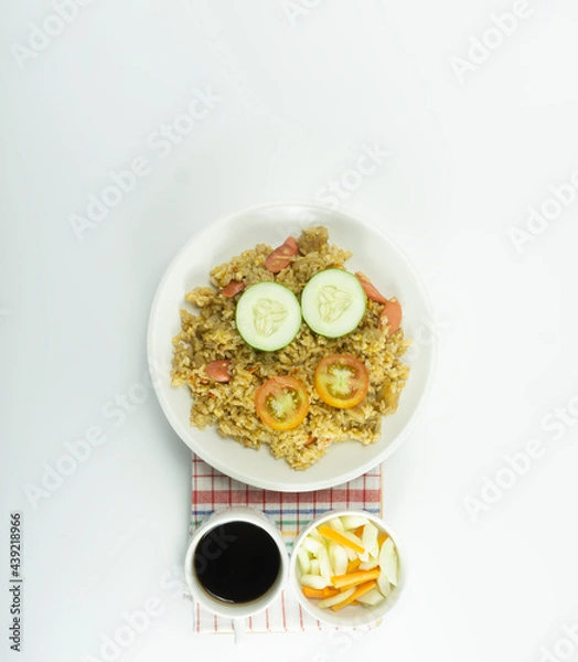 Fototapeta Nasi goreng or Indonesian Fried rice served with fresh tomatoes and meatballs on a white ceramic plate and pickles on a white bowl on a white background