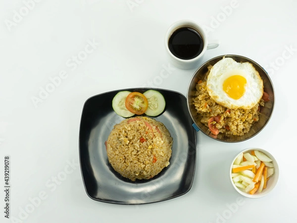 Obraz Nasi Goreng or Indonesian Fried rice served with fresh tomatoes and meatballs in a black tosca plate and pickles on a white bowl on a white background