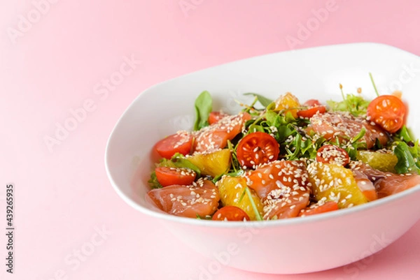 Fototapeta Fresh salad with salmon and vegetables close up in a bowl over pastel pink background.