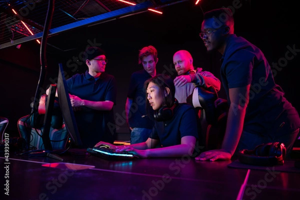 Fototapeta A cyber team of guys and a coach explains their strategy to a new team member an asian girl