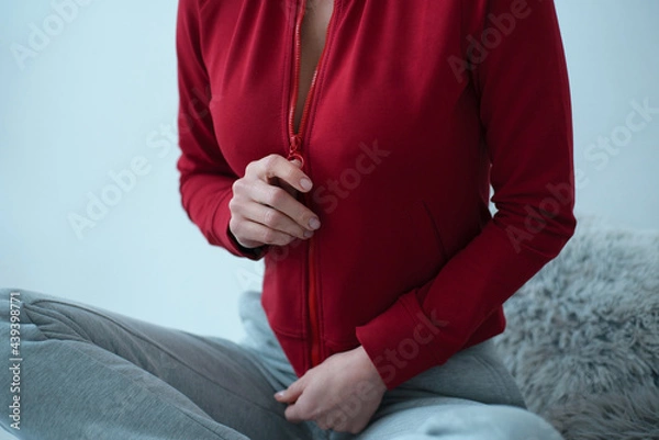 Obraz a girl without a face sitting zips a red sweater on herself with her hand