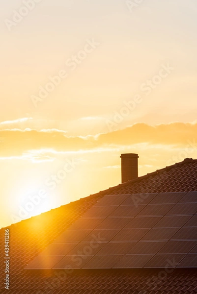 Obraz Real photo of photovoltaic panels on the roof of the house against the setting sun. Background with copy space in warm, sunny tones, perfect for solar energy materials