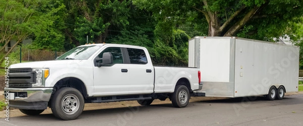 Fototapeta White pickup truck and large utility trailer parked on residential city street.