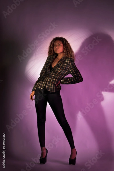 Fototapeta vertical portrait of a curly model wearing a jacket, black pants and high heel shoes in a purple backgroung