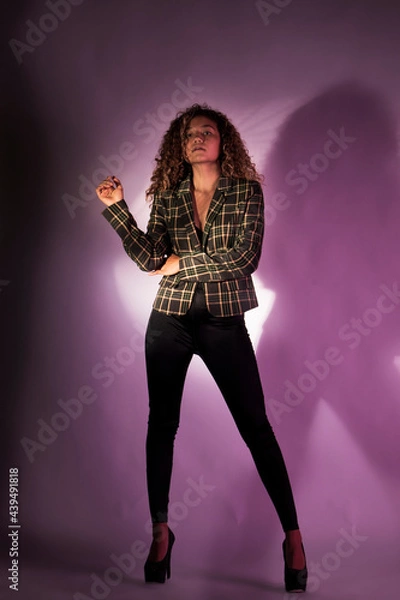 Fototapeta vertical portrait of a curly model wearing a jacket, black pants and high heel shoes in a purple backgroung